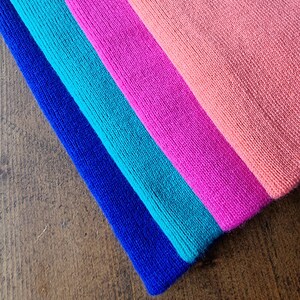 May include: Four fabric headbands in a rainbow color scheme. The headbands are stacked on top of each other, with the blue headband on the bottom and the pink headband on top. The headbands are made of a soft, stretchy fabric.