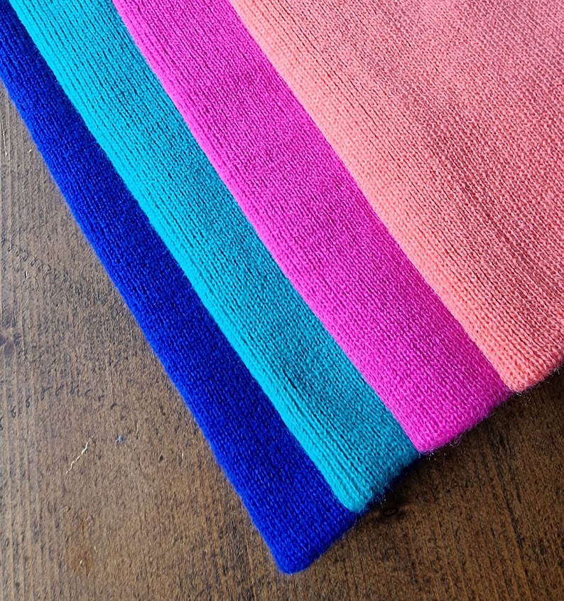 May include: Four fabric headbands in a rainbow color scheme. The headbands are stacked on top of each other, with the blue headband on the bottom and the pink headband on top. The headbands are made of a soft, stretchy fabric.