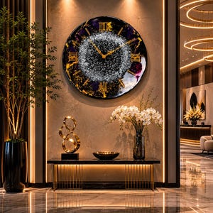 Può includere: Un grande orologio da parete rotondo con un quadrante nero, oro e viola. L'orologio presenta numeri romani e un centro scintillante. L'orologio è montato su una parete dai toni neutri sopra un tavolo nero con accenti dorati. Una scultura dorata e un vaso di fiori bianchi sono sul tavolo.