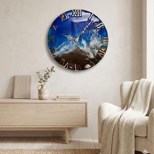 Könnte beinhalten: Eine runde Wanduhr mit einem blau-weißen Harzdesign, das an Meereswellen erinnert. Die Uhr hat goldene römische Ziffern und Zeiger. Die Uhr hängt an einer hellen Wand.