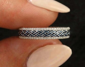 May include: A silver-toned ring featuring a central braided pattern with deep blue enamel detailing, flanked by two thin rows of small, clear, sparkling stones along the top and bottom edges of the band, creating a textured and layered appearance.