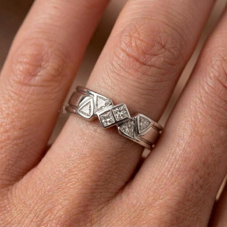 May include: A silver ring with geometric designs. The ring features a series of triangles and square-shaped stones. The ring is on a finger, and the design is modern and eye-catching.