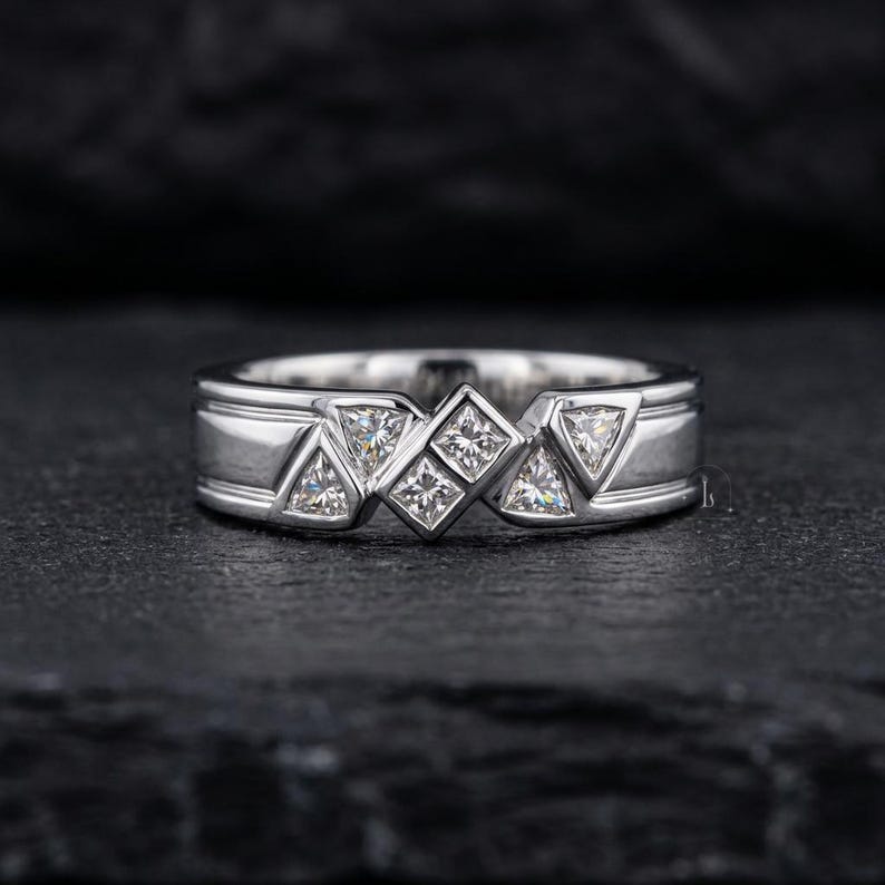 May include: A silver ring with a geometric design. The ring features square and triangular-shaped clear stones set in a band with a rectangular design. The ring is displayed on a dark surface.