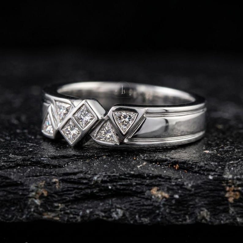 May include: A silver ring with a geometric design featuring square and triangular-cut gemstones. The ring has a polished finish and a band with a grooved detail. The gemstones are set in a repeating pattern across the top of the ring.