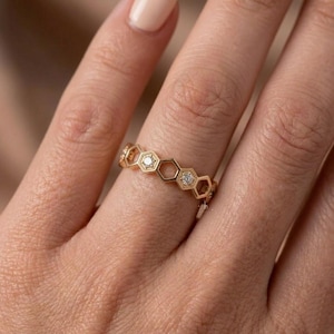 Pu&ograve; includere: Un anello dorato con un design a nido d'ape. Ogni esagono &egrave; bordato d'oro e contiene un piccolo diamante scintillante. L'anello &egrave; indossato su un dito, mettendo in risalto i suoi dettagli e il suo stile elegante.