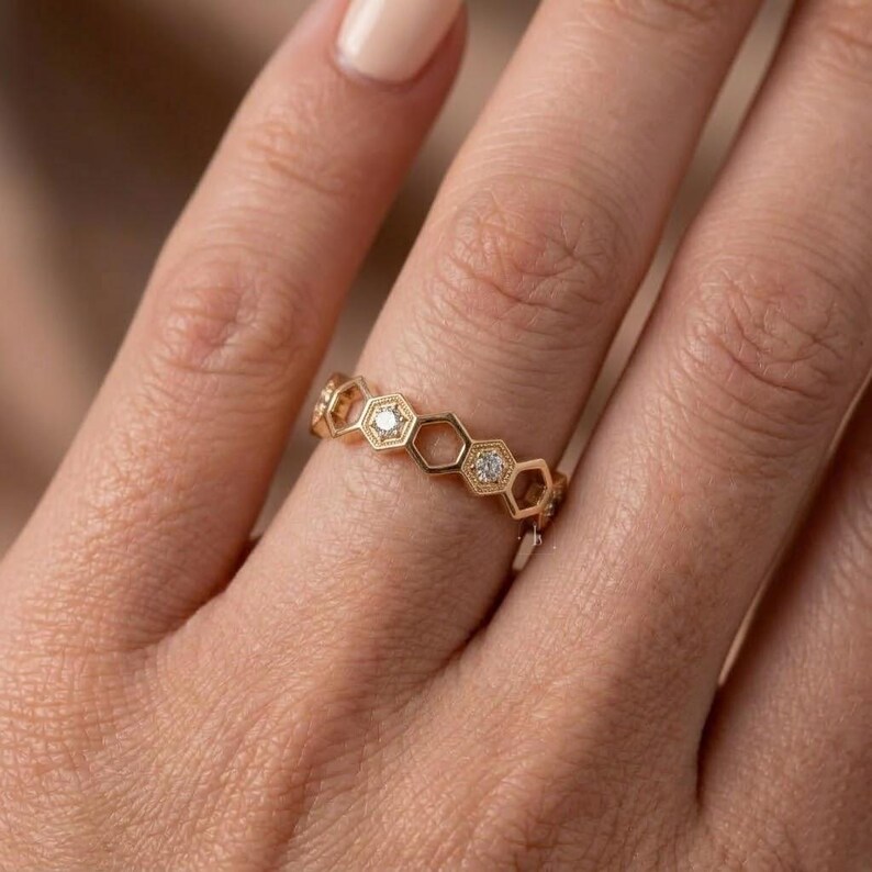 Pu&ograve; includere: Un anello dorato con un design a nido d'ape. Ogni esagono &egrave; bordato d'oro e contiene un piccolo diamante scintillante. L'anello &egrave; indossato su un dito, mettendo in risalto i suoi dettagli e il suo stile elegante.