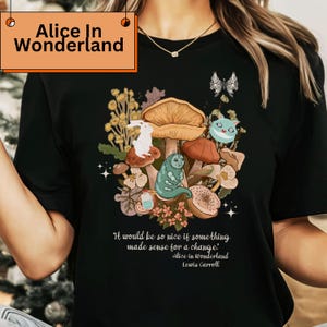Peut inclure: T-shirt noir avec une illustration color&eacute;e d'Alice au pays des merveilles. Le motif comprend un lapin blanc, une chenille, des champignons et la citation "It would be so nice if something made sense for a change." Le texte "Alice in Wonderland" et "Lewis Carroll" est &eacute;galement inclus.