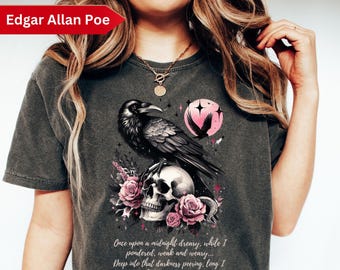 May include: A dark gray t-shirt with a black raven perched on a skull surrounded by pink roses. The text "Once upon a midnight dreary, while I pondered, weak and weary... Deep into that darkness peering, long I stood there wondering, fearing... Edgar Allan Poe" is printed on the shirt.