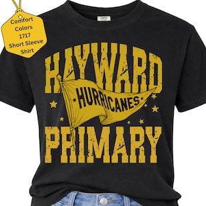 May include: A black short-sleeve t-shirt featuring yellow distressed text that reads Hayward Hurricanes Primary. A yellow pennant flag graphic is centered between the words. A yellow tag in the top left corner displays Comfort Colors 1717 Short Sleeve Shirt.
