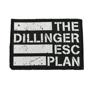 May include: Black rectangular patch with white text that reads "THE DILLINGER ESC PLAN". The text is in a bold, sans-serif font. The patch has a distressed, worn look with white horizontal bars.
