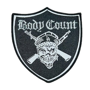 May include: Black and white patch with a shield shape. The patch features the text "Body Count" in a gothic font, a skull wearing a hat with "LA" on it, and crossed rifles. The patch has a white border.