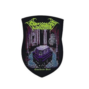 May include: A shield-shaped embroidered patch with a black border. The design features a purple sarcophagus in a dark chamber with a light green logo at the top reading Gorguts and the text Considered Dead in light green at the bottom.