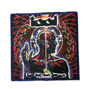 May include: Square patch with a black border featuring a detailed illustration. The design includes a human profile, a central spine, and the band's logo at the top. The background is a mix of colours, including red, blue, and purple, with the text "La teca lums".