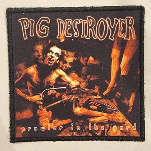 Op de afbeelding: Vierkant zwart embleem met de woorden "PIG DESTROYER" in witte en oranje letters. Het embleem toont een donkere, grafische illustratie van figuren en de tekst "prowler in the yard" in witte letters.