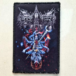 Pode incluir: Um patch retangular preto com uma ilustração detalhada de uma divindade azul com vários braços, rodeada por chamas e elementos celestes. O patch apresenta texto em uma fonte estilizada na parte superior. As bordas são finalizadas com uma borda preta desfiada.