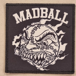 May include: Black square patch with the word "MADBALL" in white block letters above a cartoon baseball with an angry face, stitched seams, and a cigar. The baseball is surrounded by white flames.