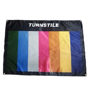 May include: A rectangular black banner with the word "TURNSTILE" in white block letters at the top. The banner features vertical stripes in green, blue, white, pink, orange, yellow, and blue. The banner has grommets in each corner.