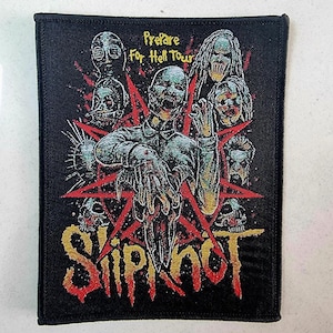 May include: Black and red embroidered patch with the band name "Slipknot" in gold lettering. The patch features a pentagram with a skull in the center and several figures with demonic features around it. The text "Prepare for Hell Tour" is visible at the top of the patch.