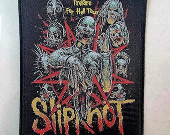 May include: A black and red embroidered patch featuring the band name "Slipknot" in gold lettering. The patch depicts a pentagram with a skull at its centre and several figures with demonic features surrounding it. The text "Prepare for Hell Tour" is visible at the top of the patch.