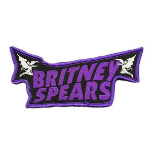 May include: A black and purple embroidered patch with the words "BRITNEY SPEARS" in purple. The patch has a purple border and white illustrations of winged figures at each end.