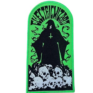 Pode incluir: Um patch verde e preto com o texto "ELECTRIC WIZARD". Apresenta uma figura encapuzada com uma cruz, sobre uma pilha de crânios, com desenhos de fumaça verde. Borda verde.