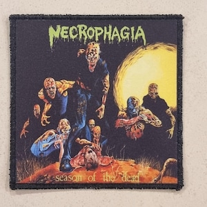 Può includere: Toppa quadrata con bordo nero con il nome della band "Necrophagia" in verde sopra una grafica di zombi e la scritta "season of the dead". L'opera d'arte ha un tema oscuro e horror.