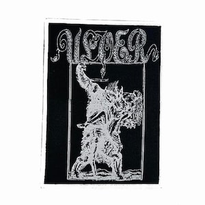 May include: A rectangular black and white embroidered patch featuring the text ULVER at the top in a stylized font. Below the text, a detailed illustration depicts a large, shaggy creature standing within a framed border on a black background.