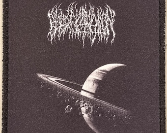 May include: Black square patch featuring a white, stylized band logo above a black and white illustration of a planet with rings. The planet has a crescent shape and is surrounded by small, dark objects.