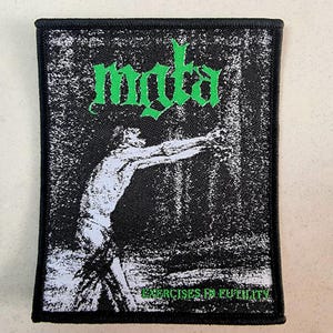 Pode incluir: Patch preto e branco com texto verde que diz "MYKTA" e "EXERCISES IN FUTILITY". O patch apresenta uma imagem estilizada de uma pessoa estendendo os braços.