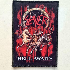 May include: Black patch featuring the band name "SLAYER" above a graphic of figures in a hellish scene, with the words "HELL AWAITS" below. The patch has a red background and a black border.