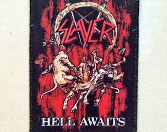 May include: Black patch with the band name "SLAYER" above a hellish scene graphic, and the words "HELL AWAITS" below. The patch has a red background and a black border with frayed edges.