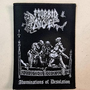 May include: Black and white embroidered patch with the band name "Morbid Angel" and the text "Abominations of Desolation". The patch features a graphic of a demonic scene with figures in a bed.
