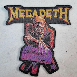 May include: Embroidered patch with the band name "MEGADETH" in gold lettering above a skeletal figure in a suit. The figure holds a purple sign that reads "FOR SALE". The patch has a black border.