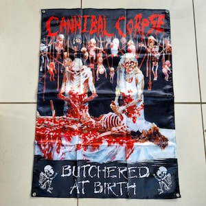 Puede incluir: Bandera negra con el nombre de la banda "Cannibal Corpse" en rojo, que representa una escena sangrienta. La bandera incluye el texto "Butchered at Birth" en blanco, y figuras esqueléticas.