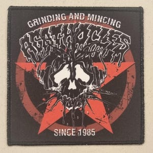 May include: Black and red patch featuring a skull design. The skull is white with black detailing, set against a red star. The text "GRINDING AND MINCING DEATH CYCLES" and "SINCE 1985" are displayed in white.