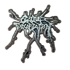 Puede incluir: Un pin metálico plateado con la palabra "DECAPITATED" en una fuente estilizada. El pin tiene un diseño abstracto con acentos grises oscuros y grises claros, y un contorno negro. El pin está sobre un fondo blanco.