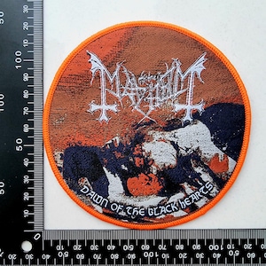 Könnte beinhalten: Runder Aufnäher mit orangefarbenem Rand und einem Used-Design. Der Aufnäher zeigt den Bandnamen "Mayhem" in weißer, gotischer Schrift über einem grafischen Bild und dem Text "Dawn of the Black Hearts".