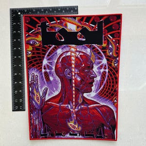 May include: A large, rectangular patch with a red border. The patch features a detailed illustration of a human head and torso in shades of red and purple, with the band's logo at the top. The patch measures approximately 12 inches in height.