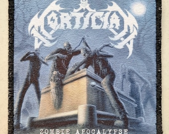 May include: Square patch with a black border. The design features a zombie apocalypse scene with the band name "Mortician" in white, a skull, and zombie figures. The text "ZOMBIE APOCALYPSE" is at the bottom of the patch.
