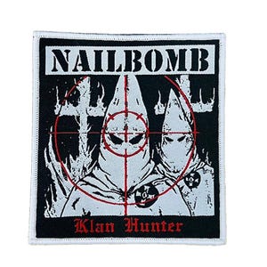 Könnte beinhalten: Quadratischer Aufnäher mit dem Wort "NAILBOMB" in weißen Blockbuchstaben über einer Grafik von zwei Kapuzenfiguren in Weiß, die von einem roten Fadenkreuz anvisiert werden. Der Text "Klan Hunter" steht in roter Schrift unter den Figuren auf schwarzem Hintergrund.