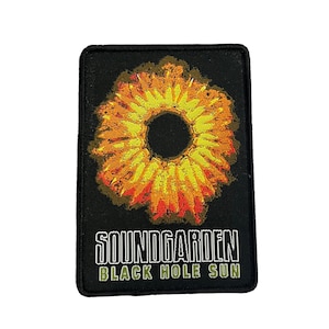 Può includere: Toppa nera rettangolare con un disegno stilizzato del sole nei toni del giallo, arancione e rosso. La toppa presenta il testo "SOUNDGARDEN" e "BLACK HOLE SUN" in bianco e verde, un design associato alla band.