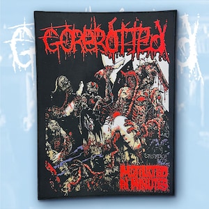 May include: A rectangular black fabric patch featuring a graphic illustration of multiple zombie-like figures in red, white, and black. The text GOREROTTED appears in a stylized red font at the top, with MOTILATED IN MINUTES printed at the bottom.