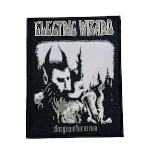 以下が含まれることがあります： 上部に白い文字でELECTRIC WIZARD、下部にdopethroneと記された長方形の黒い刺繍ワッペン。中央には、黒い背景に煙のようなディテールを持つ角のある人物の白いグラフィックイラストが描かれています。