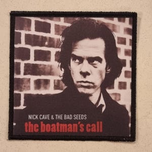 Puede incluir: Parche cuadrado con un retrato en tonos sepia de Nick Cave sobre un fondo de pared de ladrillos. Los textos "NICK CAVE & THE BAD SEEDS" y "the boatman's call" están impresos en rojo y blanco. El parche tiene un borde negro.