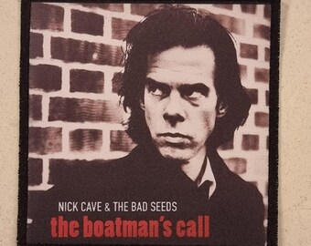 May include: Square patch with a sepia-toned image of Nick Cave, set against a brick wall. The text "NICK CAVE & THE BAD SEEDS" and "the boatman's call" are printed in red and white. The patch has a black border.