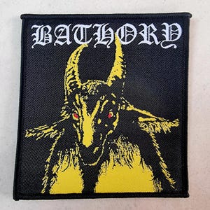 May include: Black and yellow embroidered patch with the band name "BATHORY" in white lettering and a yellow goat head with red eyes.