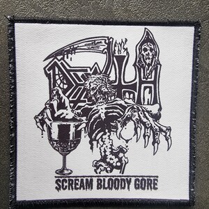 Op de afbeelding: Een vierkante, witte patch met een zwarte rand. Het heeft een zwart-wit illustratie van een skeletfiguur, een beker en de tekst "SCREAM BLOODY GORE". De patch heeft een gestikte rand.