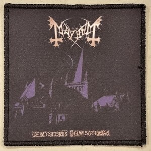 May include: Black patch featuring the band name "Mayhem" in a stylized white font. Below the logo is a purple and black illustration of a church. The text "De Mysteriis Dom Sathanas" is at the bottom.