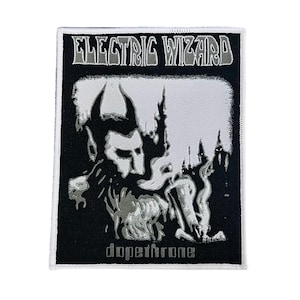 May include: A rectangular embroidered patch featuring a black and white graphic design. The text ELECTRIC WIZARD appears at the top, and the word dopethrone is at the bottom. The central image depicts a horned figure with smoke-like details.