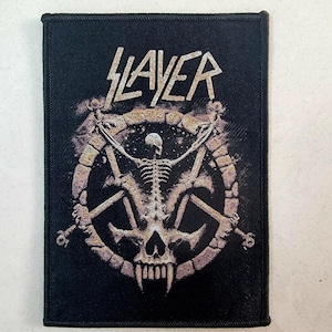Puede incluir: Parche bordado en blanco y negro con la palabra "Slayer" en una fuente estilizada. El parche presenta una figura esquelética con una cabeza de calavera, rodeada de un diseño circular.